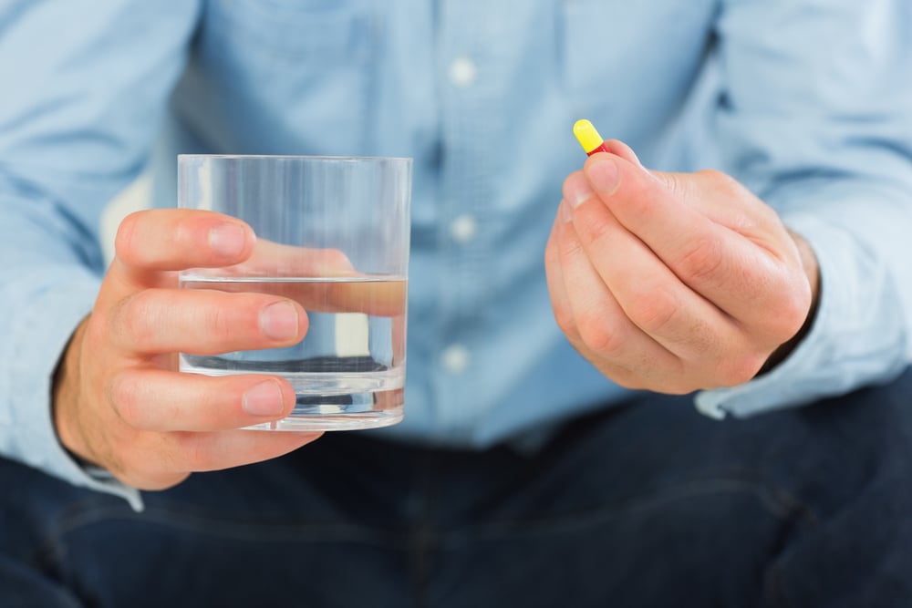 Persona che tiene un bicchiere d'acqua in una mano e una capsula nell'altra, primo piano. Persona che tiene un bicchiere d'acqua in una mano e una capsula nell'altra, primo piano.