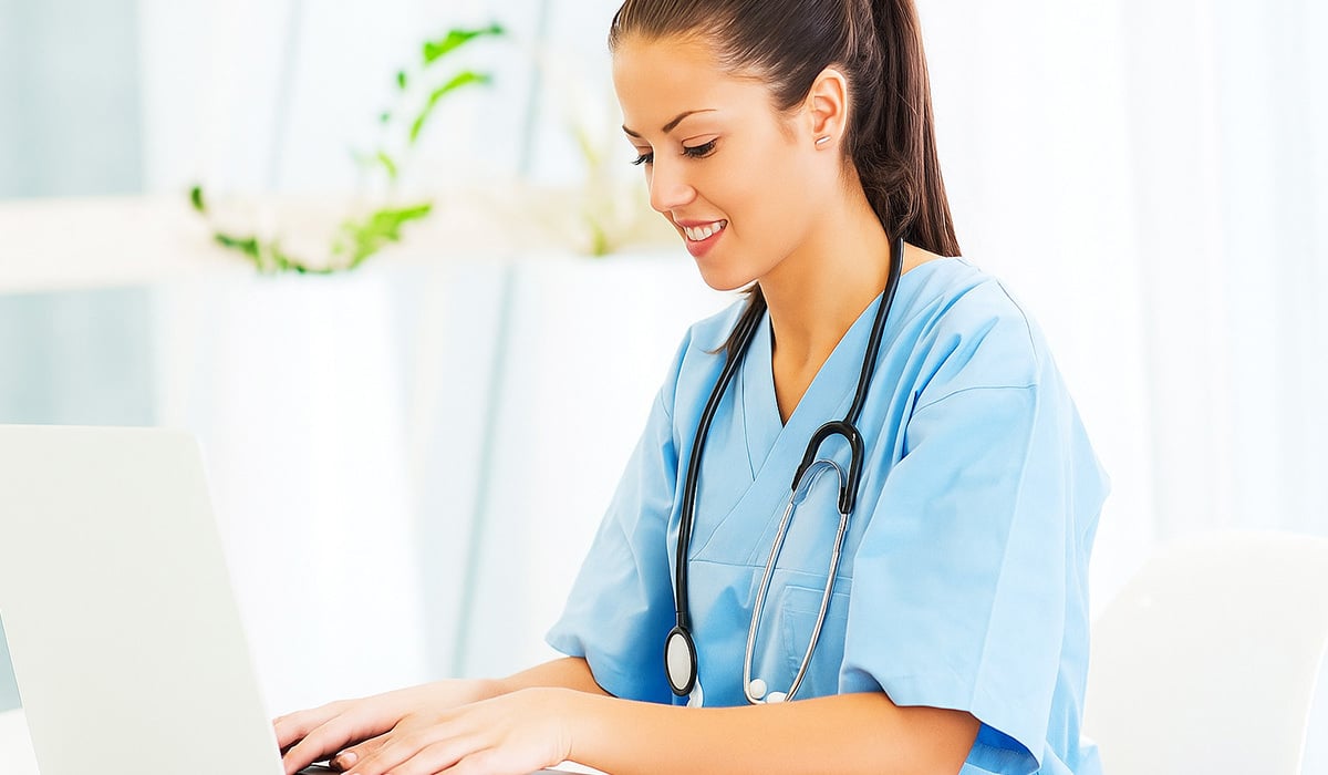 A doctor with a stethoscope works on the computer entering health data.