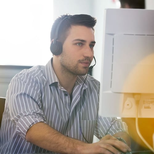 Ein Mann in gestreiftem Hemd mit Headset arbeitet konzentriert an einem Computer – Darstellung von Supportmitarbeiter für E-Voting-Dienste.