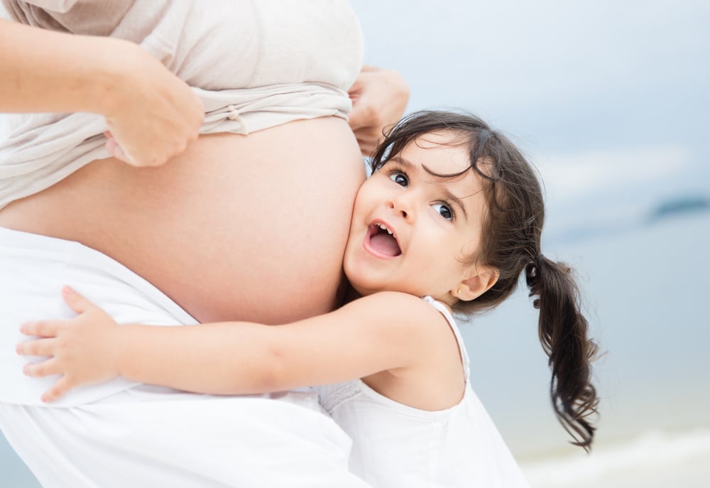 Una bambina abbraccia il ventre di una donna incinta e appoggia la testa con un sorriso. Una bambina abbraccia il ventre di una donna incinta e appoggia la testa con un sorriso.