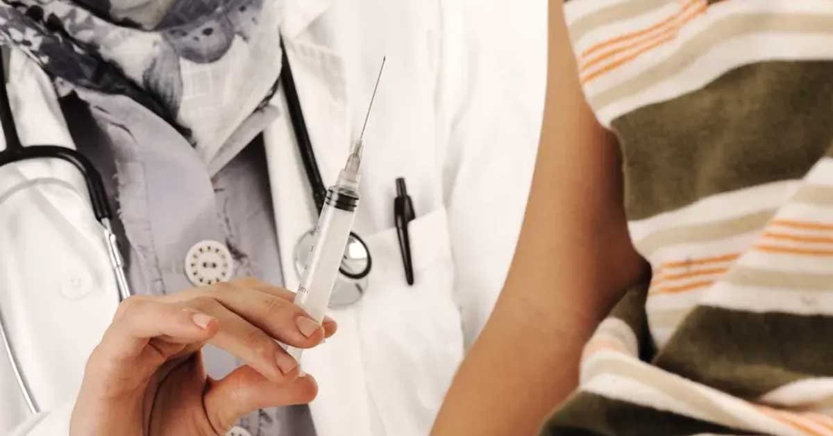 A healthcare professional in a white coat holds a syringe, ready for an injection. Next to them is the arm of a person wearing a short-sleeved striped shirt. A healthcare professional in a white coat holds a syringe, ready for an injection. Next to them is the arm of a person wearing a short-sleeved striped shirt.